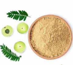 Amla powder in a bowl with amla fruit and leaves for Ayurvedic hair growth and scalp care.