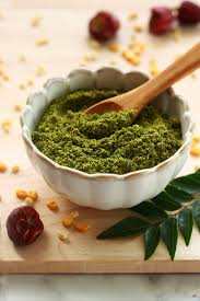 Parijata Herbs Curry Leaves Powder in a white bowl with a wooden spoon.